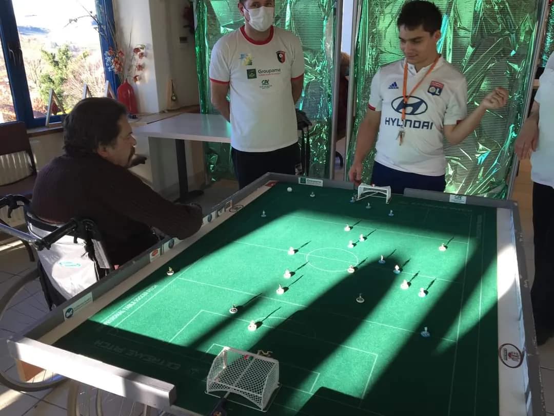 Un participant assis joue au football de table face aux joueurs du club