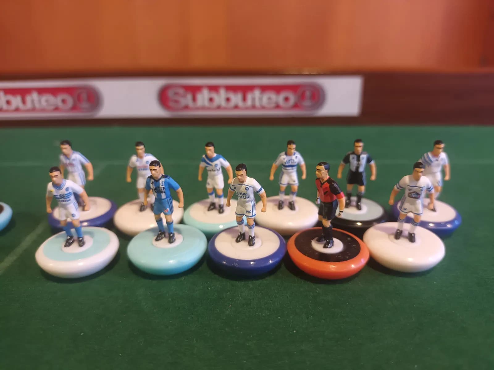 Figurines peintes aux couleurs de l'Olympique de Marseille, alignées devant une bande « Subbuteo »